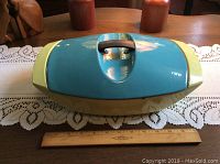 Top view of the enamel cast iron casserole with lid, showing blue and yellow color scheme and handle on lid. Ruler placed in front for size reference.