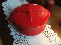 Full view of red enamel Dutch oven with spider handle lid on white lace tablecloth.