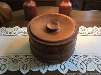Closed teak wood ice bucket with lid and knob handle, displayed on wooden surface with lace table runner.