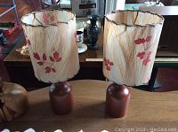 Photo of both teak mid century table lamps with fabric floral shades placed side by side on wooden table.
