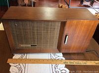 Full front view of Panasonic radio with wooden cabinet, showing woven speaker grille, door, and scale ruler for size reference.