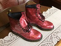Pair of red metallic Dr. Martens AirWair boots with black laces and yellow stitching on a wooden surface.