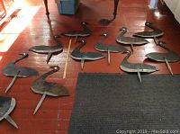 11 flat painted tin goose decoys with wooden stakes, arranged on a red floor.