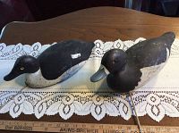 Two wooden antique duck decoys displayed on lace cloth on a wooden table showing overall size and condition.