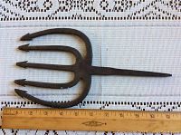 Top-down photo of antique hand-forged cast iron spear fishing fork next to a ruler showing length about 9 inches