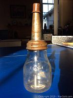 Full view of clear 500ml glass oil bottle with metal lid attached, sitting on a table.