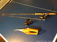 Two fishing rods with Garcia Mitchell reels and one yellow-orange Pocket Fisherman device laid out on a dark surface.