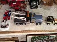 Photo showing large blue and white metal Nylint Tow Truck, small white metal Tonka Jeep, and a metal Spiderman thermometer on a table with a wooden ruler for scale.