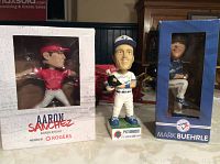 Three Blue Jays bobbleheads displayed together on a surface. Pat Borders is out of the box; Aaron Sanchez and Mark Buehrle are in original packaging.