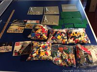 Photo showing bags of assorted LEGO pieces alongside baseplates and several LEGO instruction manuals.