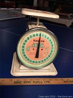 Front close-up photo showing round dial with the brand and baby-themed artwork on the face, and the metal base.