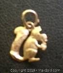 Close-up photo of a small gold charm shaped like a squirrel, shows the charm's details and loop for attachment.