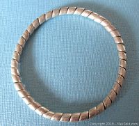 Full view of the sterling silver ribbon style bangle bracelet on blue textured background.