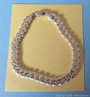 Entire bracelet laid out on yellow and blue textured background showing the full Figaro chain style and clasp.