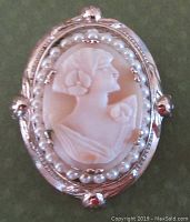 Front view of the oval brooch showing the shell cameo of a lady's profile in gold tone metal frame surrounded by intact imitation round pearls.