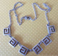 Photo of vintage sterling silver Greek key link necklace laid flat showing five square Greek key motif links and linked chain with clasp.