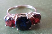 Top angled view showing three round stones: central deep blue gemstone flanked by two red garnets in 14K yellow gold setting.