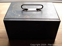 Closed camphor wood carrying case with metal handle on top and faint stenciled dragon design visible