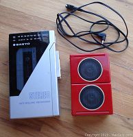 Front view of grey metal Sanyo cassette player with black tuning display and red external speakers with connecting cord.