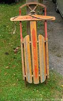 Full view of the vintage wooden Sno-Flight sleigh showing the entire body and handlebar with red metal runners on grass.