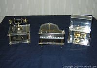 Three acrylic music boxes arranged on dark cloth: telephone, grand piano, upright piano