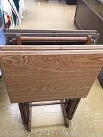 Four vintage wooden foldable TV trays stored upright inside a wooden footed rack.