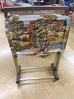 Metal TV tray with retro fall scenery art showing trees, river, hills, and cottage in fall colors on a metal stand with wheels.