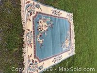 Blue and dusty rose wool rug laid flat showing full pattern and tasseled edges on grass surface.