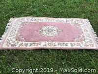 Full view of rectangular pink and beige floral wool rug laid on grass showing overall design, colors, and size.