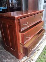 Front angle view showing three drawers of the chest, top drawer slightly open revealing interior, wood grain and antiqued finish visible