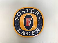 Front view of round Foster's Lager beer sign on white wall, showing logo details and colors clearly.