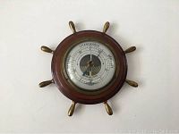 Full view of the circular wood and brass barometer with ship wheel design.