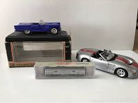 Purple Thunderbird 1/24 scale model on black display box missing one side mirror, with silver and red Shelby 1/18 scale car beside it, and Walthers train baggage car in plastic box in front.