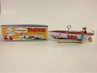 Photo showing the Popeye tin speedboat alongside its original colorful box with vintage cartoon artwork.