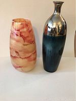 Two decorative vases against white backdrop: orange marbled glass vase and blue/silver vase with metallic top and dark blue bottom.