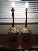 Two mid century table lamps lit and side by side showing overall height, shape and design.