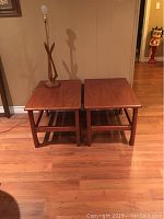 Two mid century solid wood side tables side by side, with a wood and brass lamp placed on one of them showing the whole set and relative size.