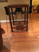 Wooden bar height table with four square legs and footrest bar shown from front.