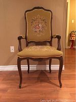 Front view of vintage wooden chair showing detailed carved frame and floral needlepoint upholstery on backrest and seat.