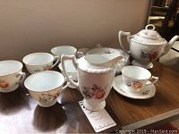 Full set of 6 tea cups, saucers, teapot, and additional components photographed on wooden table