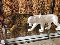 Side view of the leopard and crackled tiger figurines on glass shelf with textured background