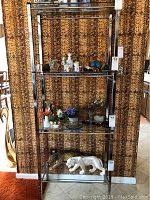 Full view of the glass shelving unit showing four shelves with various decorative items displayed, positioned against a leopard print curtain backdrop.