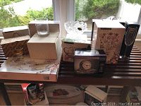 Photo showing multiple boxed crystal and glassware items arranged on a table including a boxed crystal clock, Paola Collection candy dish, Misa bowl, and other boxed serve ware and glassware items.