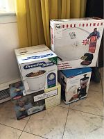 Photo showing all four boxed items stacked: George Foreman Grill, Proctor Silex crockpot, Paula Deen Toaster, and smoothie maker.