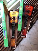Two small string guitars or ukuleles in original green boxes with 'String Guitar' text on the side. Each has sunburst finish and six strings.