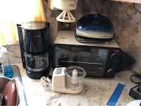 Overview photo of lot showing all kitchen appliances on a marble countertop: Proctor-Silex food processor, Krups coffee maker, Oster toaster oven, George Foreman grill, and a bottle opener.