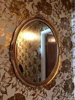 Full shot of oval vintage wall mirror hung on patterned floral wallpaper.