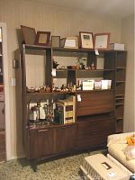 Full view of the mid-century shelving unit against a wall with various decorative items placed on shelves, a mirror section on the left, and interior contents.