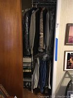 Photo showing multiple men's jackets hanging on a rod, with jeans and slacks hanging below and some shoes on the bottom of the closet.
