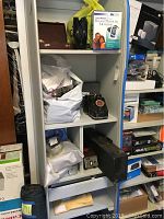 Full view of metal shelf with various vintage medical equipment including bags of supplies, vintage telephone, electronic device, and more.